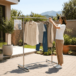 Woman adjusting Double Rail Retractable Clothes Rack outdoors with hanging clothes and accessories.