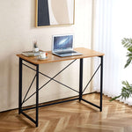 Minimalist Computer Desk with X-Frame Design featuring a laptop, plants, and a modern aesthetic in a cozy setting.