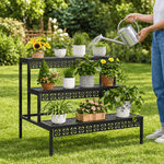 Person watering potted plants arranged on a black stepped metal plant stand