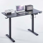 Electric Standing Desk in black with laptop, books, and speaker showcasing ergonomic design for modern workspaces.