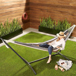 Woman relaxing in a Double Hammock with Steel Stand on grass, enjoying outdoor space with vibrant stripes.