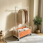 Steel Clothing Rack with Shelves & Wheels holding garments in a stylish interior setting with a plant.
