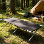 Heavy-Duty Portable Folding Camping Stretcher set up in a forest clearing near a tent.