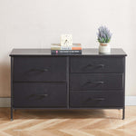 Black dresser with three drawers on a wooden floor against a white wall