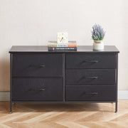 Black dresser with three drawers on a wooden floor against a white wall