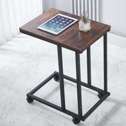 Wooden side table with wheels, tablet, and plant on a white floor.| Artisansa SA