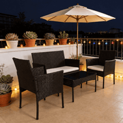 Patio Furniture Set 4 Piece PE Rattan arranged on a balcony with an umbrella, potted plants, and decorative lights.