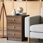 Modern 3-Drawer Nightstand with Gold Handles placed next to a grey sofa in a contemporary living room setting.