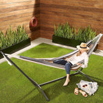 Woman relaxing in a Double Hammock with Steel Stand on grass, enjoying outdoor space with vibrant stripes.
