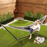 Woman relaxing in a Double Hammock with Steel Stand on grass, enjoying outdoor space with vibrant stripes.