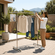 Woman adjusting Double Rail Retractable Clothes Rack outdoors with hanging clothes and accessories.