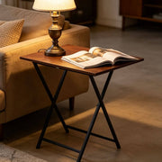 Rustic folding TV tray table beside a sofa with a lamp and a magazine for versatile use and easy storage.