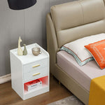 Modern LED Pedestal with open shelf beside a bed, featuring drawers and elegant decor accents.