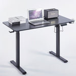 Electric Standing Desk in black with laptop, books, and speaker showcasing ergonomic design for modern workspaces.