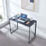 Black folding computer desk with laptop beside a bright window