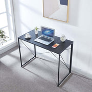 Black folding computer desk with laptop beside a bright window