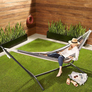 Woman relaxing in a Double Hammock with Steel Stand on grass, enjoying outdoor space with vibrant stripes.