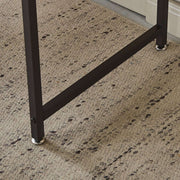 Close-up of the sturdy leg and support bar of a modern computer desk on a textured carpet.