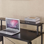 Modern computer desk with power outlets, featuring a laptop and stacked books on its surface.