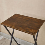 Top view of a rustic folding TV tray table with a wooden surface and black metal legs.